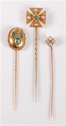 Lot 2508 - Three stick pins: to include an oval emerald...