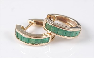 Lot 2645 - A pair of yellow metal and emerald huggy hoop...