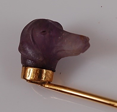 Lot 1205 - A yellow metal stick pin featuring a carved...