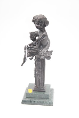 Lot 29 - A bronzed figure of putti in seated pose upon...